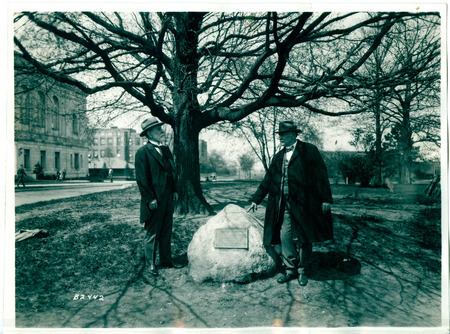 A black and white photograph of Dr. W. T. Hornaday standing with Dr. L. H. Pammel near a rock dedicated to Hornaday's contributions to zoology and conservation at Iowa State University.