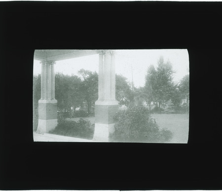 Pillars of house and yard with trees and shrubs.