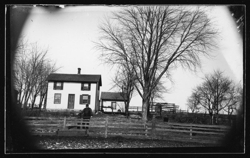 The Bussen farm, east of Grand Mound, Iowa. A man is at a pump near the fence at the front of the yard.