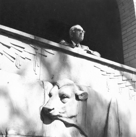 Christian Petersen standing behind the "History of Dairying" sculpture (terra-cotta, 1934), installed at the Dairy Industry Building (later the Food Sciences Building) on the Iowa State University campus. Cco: Silver gelatin photograph on board