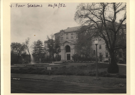 Photograph of the North facade of the Memorial Union at Iowa State University. A dirt road can be seen along with the three-spout fountain before the addition of Christian Petersen sculptures.