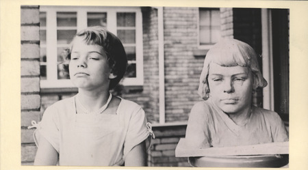 A child, presumably Andrea Johnson, poses next to a portrait bust by Christian Petersen in 1947.