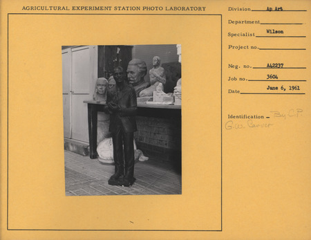 Photograph of a sculpture of George Washington Carver sculpted by Christian Petersen. A small maquette of "Conversations," a bas-relief of children, "Jens Jensen," and two unidentified portraits are seen in the background.