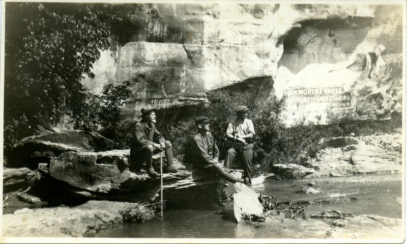 Carl Fritz Henning (on the left with the walking stick), Walter Rosene (in the middle), and Charles J. Spiker (on the right with the lunch basket) sitting by shallow water at Ledges State Park. Photograph originally titled "Photograph of Carl Fritz Henning, Walter Rosene, and Charley Spiker at Ledges State Park." Rosene provides details on back of photograph.