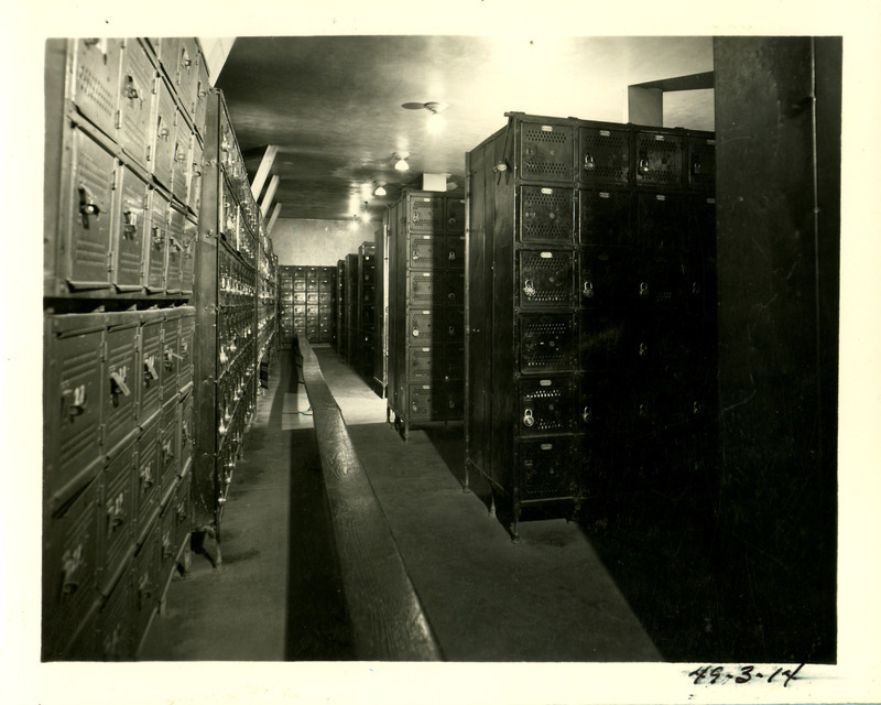 A long wooden bench runs the length of this State Gymnasium locker room and is surrounded by rows of box lockers.