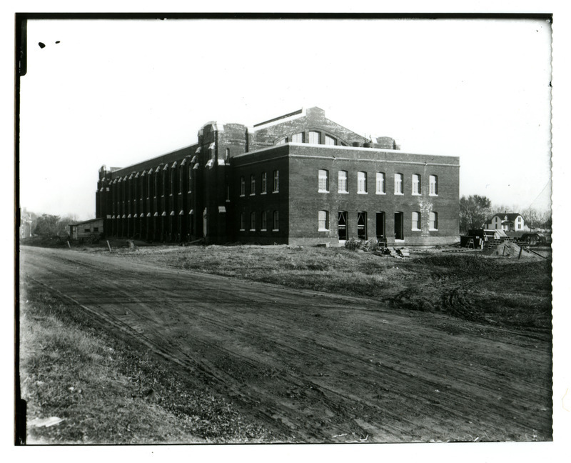 A dirt road runs along the front (north) of State Gymnasium. Work is continuing on the doors and windows on the west wing of the building. Chemical and Physical Hall is on the far left before it burnt down in 1913 and Grounds Cottage is on the right. Grounds Cottage was moved across from the Heating Plant in 1924.