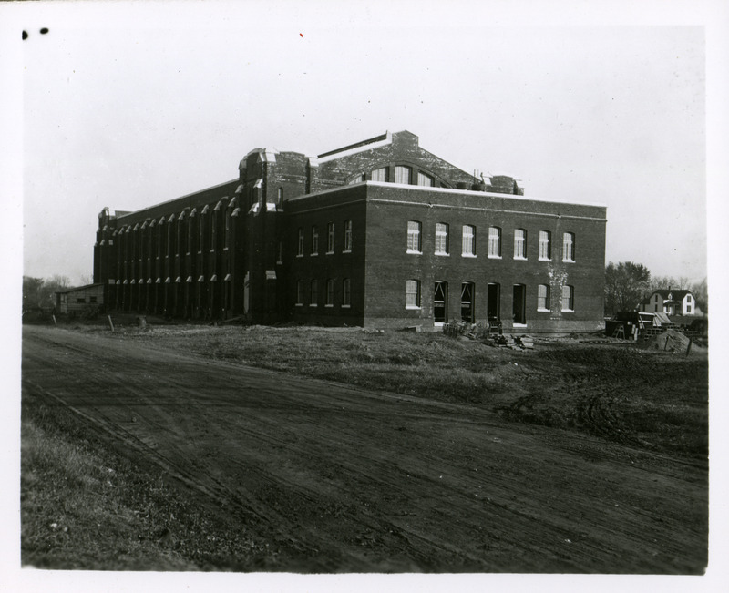 A dirt road runs along the front (north) of State Gymnasium. Work is continuing on the doors and windows on the west wing of the building. Chemical and Physical Hall is on the far left before it burnt down in 1913 and Grounds Cottage is on the right. Grounds Cottage was moved across from the Heating Plant in 1924.