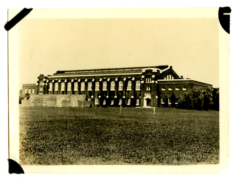 The back (south) side of State Gymnasium is viewed from the southeast side of State Field (later Clyde Williams Field). Two people are in the field and handball courts have been erected near the building.