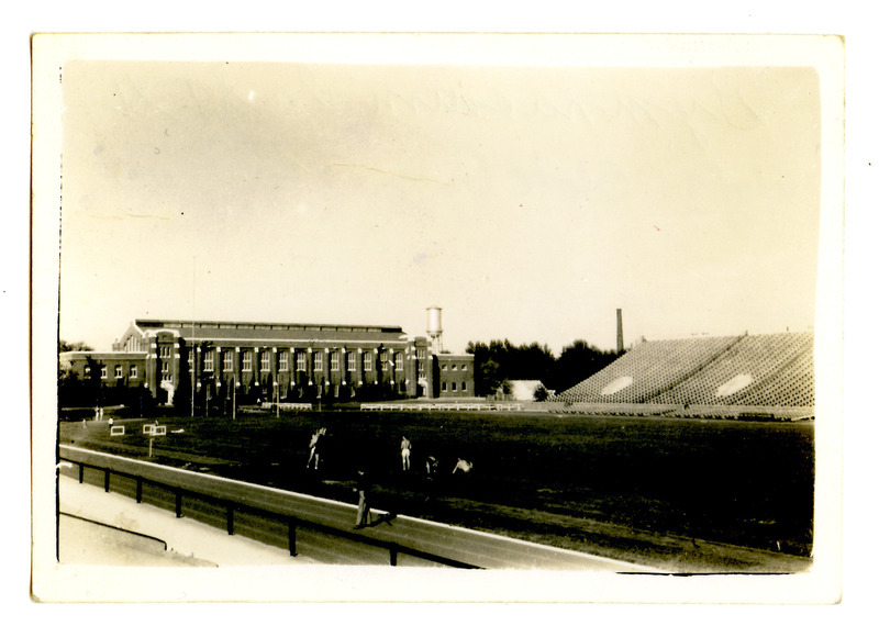 Runners stretch on the southwest side of Clyde Williams Field, viewed from the bleachers. The State Gymnasium is in the background along with the Marston Water Tower.