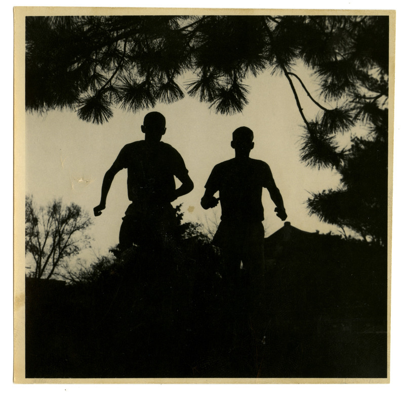 Two runners are silhouetted against trees and the top of a building that could be the State Gymnasium.