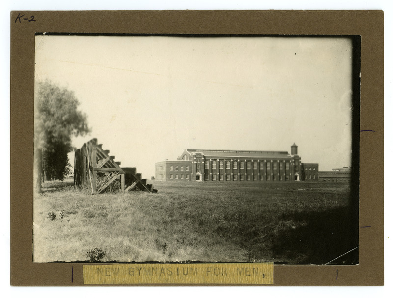 The new State Gymnasium is viewed from the southwest side of the field, with low wooden bleachers and trees on the left. The photo is labeled "New State Gymnasium for Men.".