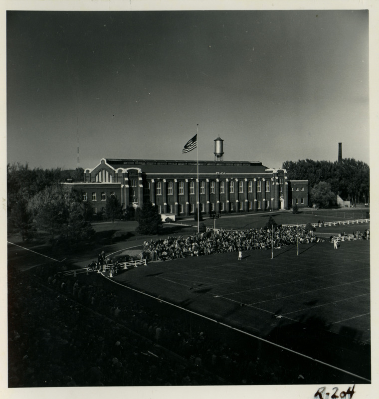 Spectators fill bleachers in the end zone of Clyde Williams Field in back (south) of the State Gymnasium, viewed from the southwest bleachers, in a dark exposure.