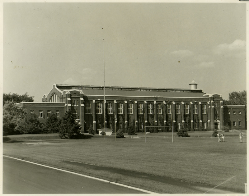 The State Gymnasium is viewed from southwest Clyde Williams Field, with three men on the field.