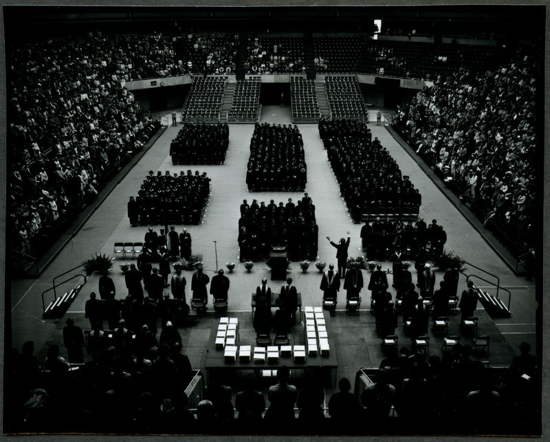 Everyone is standing directing their attention to a man with outstretched arms addressing the graduates during commencement ceremonies at Hilton Coliseum, 1978.