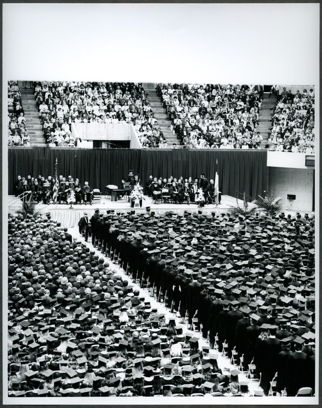 Graduates are seated at graduation ceremonies in Hilton Coliseum. Friends and family are seated in the balconies and someone is speaking at the podium, 1972.