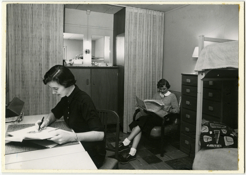 Two women college students are seen in a dorm room at Westgate Hall in 1955. The one on the left appears to be studying while the one in back reads a newspaper.