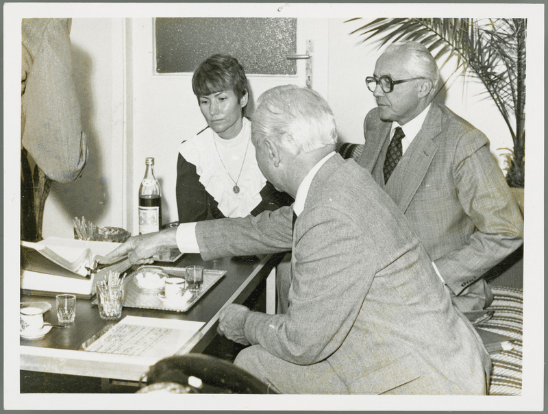 Earl O. Heady points at a book while having beverages in Hungary with Dr. Joseph Toth and a woman translator, 1979. Dr. Joseph Toth is Rector (President) of the Debrecen Agricultural University of Hungary.