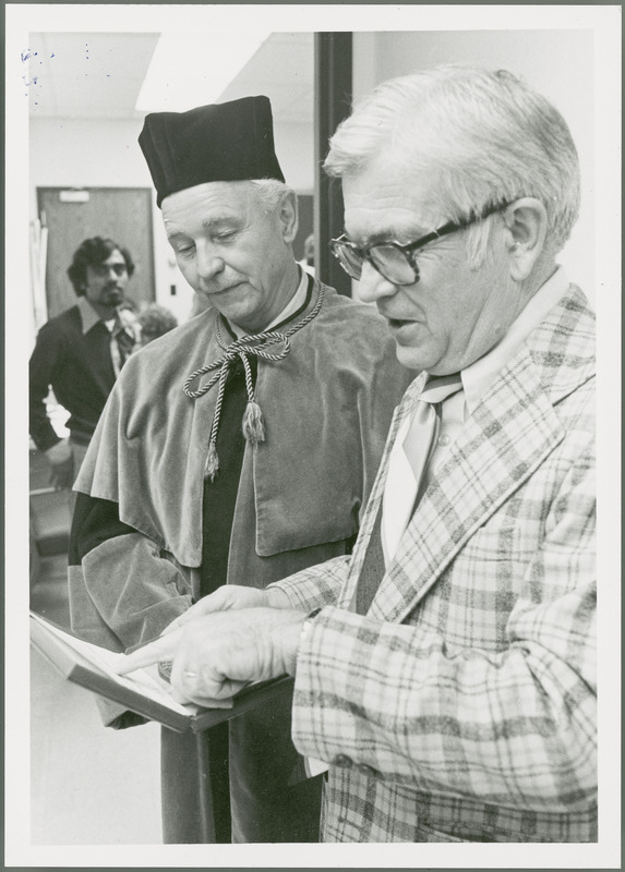 Earl O. Heady, in his Polish honorary doctorate academic robes, looks on proudly as Department of Economics Chair Raymond Beneke points at the inscription on Heady's award from the Warsaw Agricultural University, 1979.