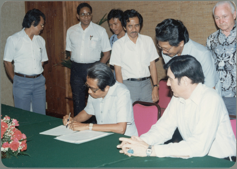 Five Indonesian men, Earl O. Heady and another American witness an Indonesian man signing the Indonesian Project Contract.