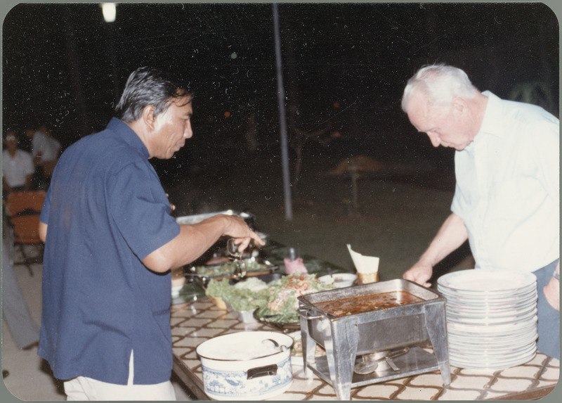 A man who resembles Somnuk Sriplung points out a food choice as Earl O. Heady makes selections in the buffet line during his visit to Thailand, April 1983.