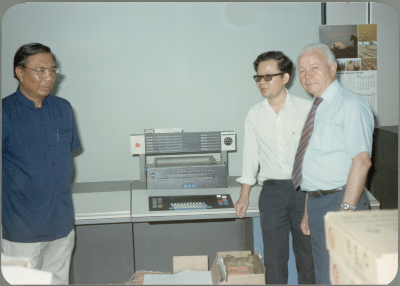 Earl O. Heady inspects upgraded equipment at the Office of Agricultural Economics computer center with office chief Somnuk Sriplung and another official, April 1983. The machine they are near appears to be an IBM keypunch machine.