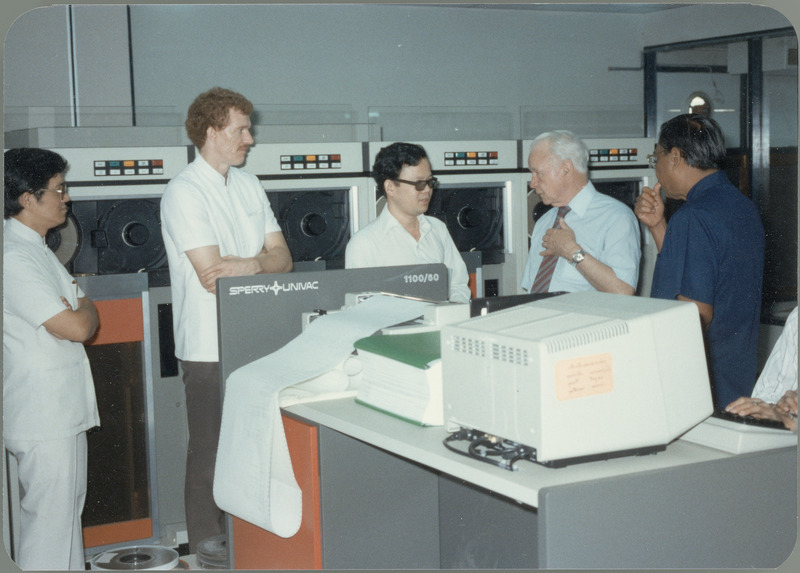 Earl O. Heady discusses new computer equipment with four men at the Office of Agricultural Economics computer center in Bangkok, Thailand, April 1983. One of the new items shown is the Sperry/Univac 1100/60 mainframe. The tall red-haired man is Gary Vocke, ISU graduate and Chief of Party for the Thai Project.