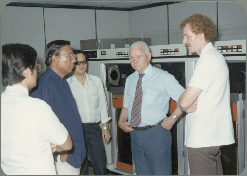 Earl O. Heady discusses new computer equipment with four men at the Office of Agricultural Economics computer center in Bangkok, Thailand, April 1983. The tall red-haired man on the right is Gary Vocke, ISU graduate and Chief of Party for the Thai Project. Second from left in blue is Somnuk Sriplung, Chief of the Office of Agricultural Economics in the Ministry of Agriculture, who earned an ISU Ph.D in agricultural economics under Earl Heady.