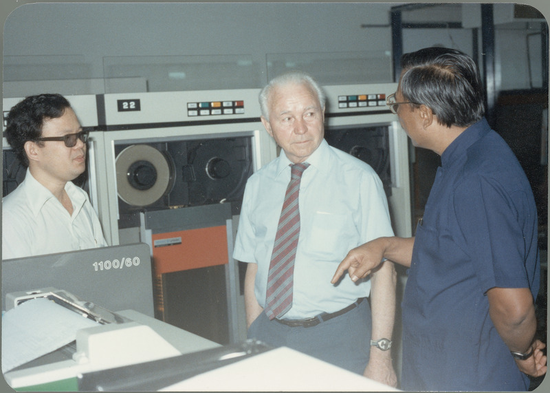 Earl O. Heady hears about upgraded equipment at the Office of Agricultural Economics computer center in Bangkok, Thailand, from office chief Somnuk Sriplung, with another official standing by, April 1983. The new Sperry/Univac 1100/60 mainframe is part of the equipment shown, with a printer operating in the foreground.