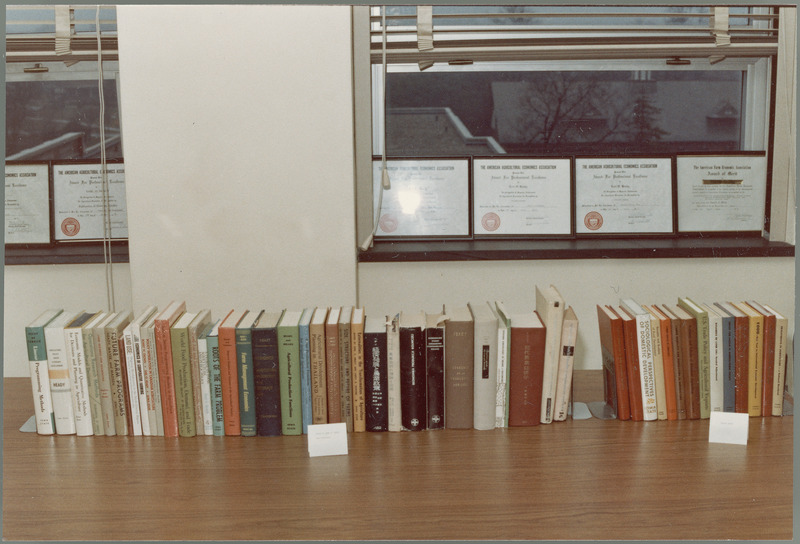 Books written by Earl Heady or CARD associates sit in a row on Earl Heady's desk, while six of his awards from the American Agricultural Economics Association are lined up in the windows behind them, August 1983.