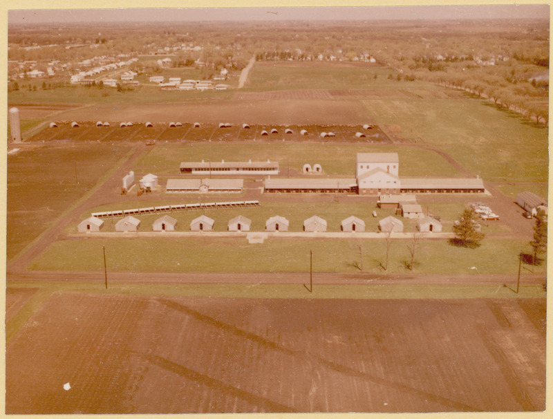 An aerial view of various farm buildings and facilities includes buildings, roads, fields and a parking lot.