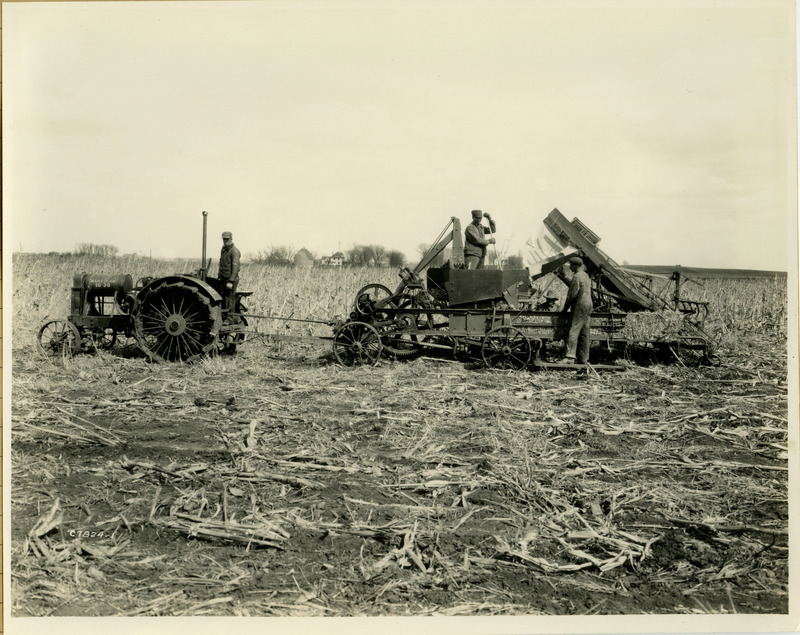 Four men are working in a corn field with a corn stalk baler. The bailer is being pulled by a Hart-Parr 16-30 tractor.