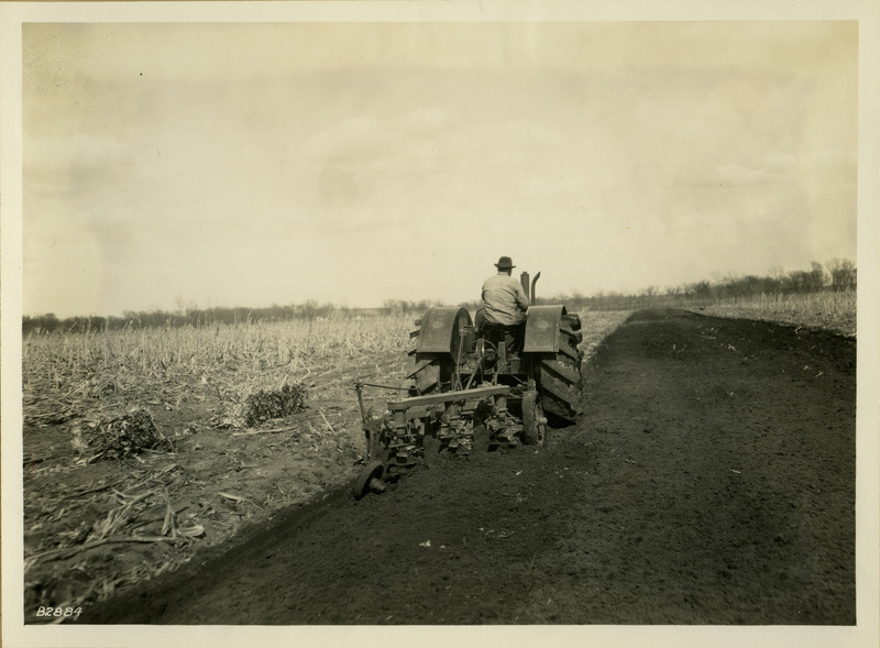 A tractor is pulling a piece of farm equipment through a partially plowed field.