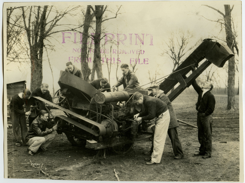 Several men are working on a large piece of farm equipment.