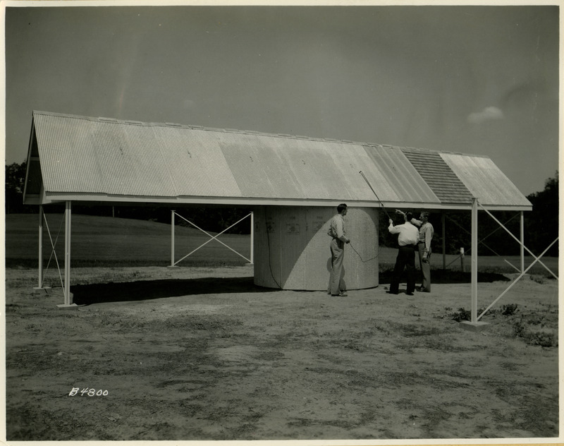 A group of three men examine the steel roof on a farm building.