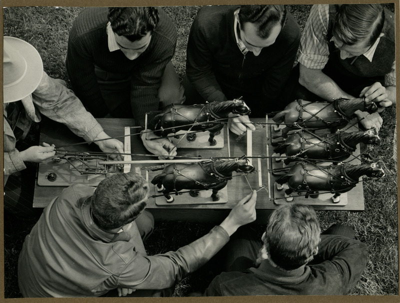 A horse hitch model with five horses is examined by a group of men.