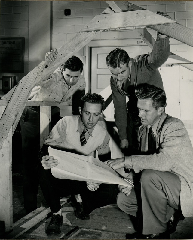 J. Bruce Liljedalh and three students study the blueprints of a wooden buildings model.