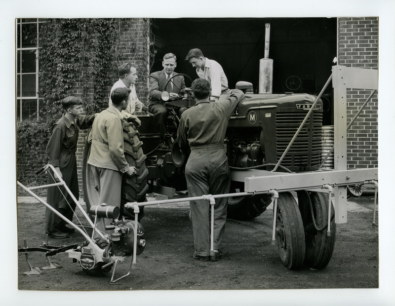 A group of students listen to an instructor explaining the use of a tractor mounted pest and weed sprayer.