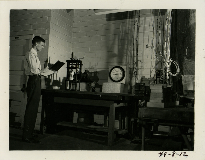 A man is standing in front of some nail testing equipment. He is recording the results of the test in a clipboard.