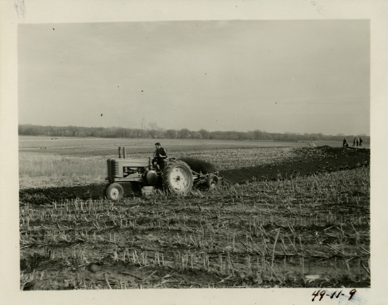 One man is driving a tractor while others look on in the distance. The Agricultural Engineering students are learning how to layout, build and check terraces on farm land for erosion control.