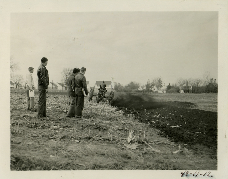 A group of individuals are observing a tractor that is engaged in building a terrace for erosion control.