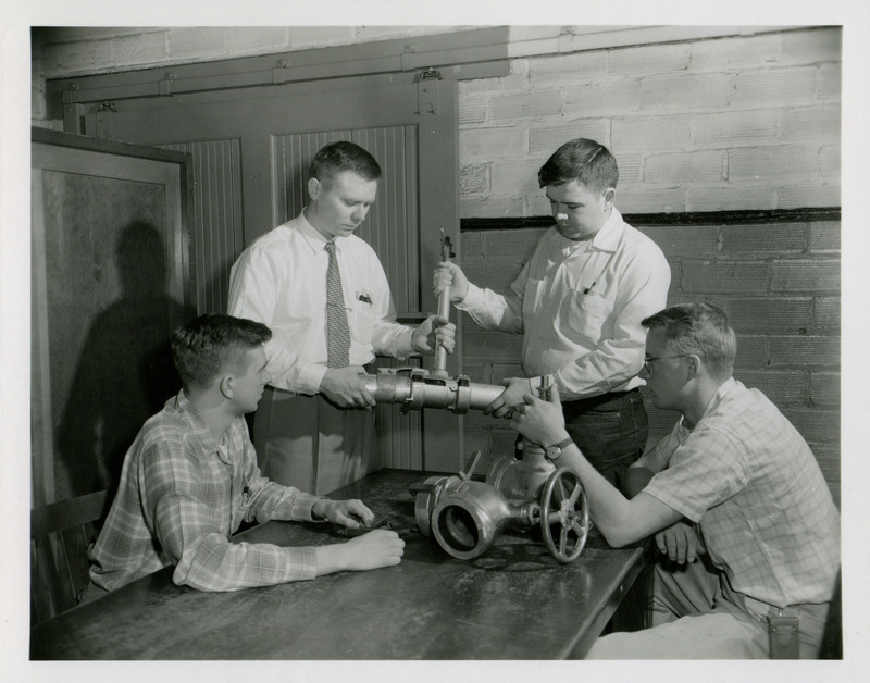 Professor Howard Johnson helps one student adjust a water hydrant fixture, while two others observe in a lab class about sprinkler irrigation equipment.