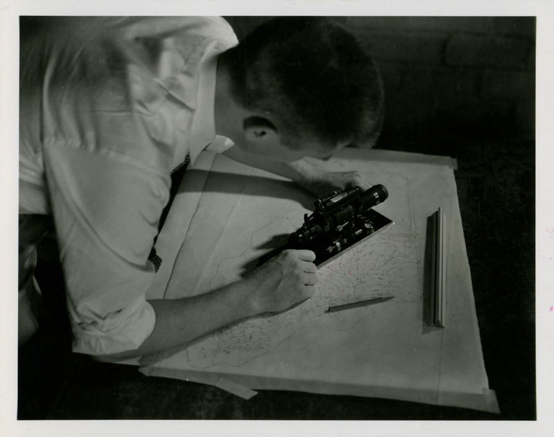 A student performs plane table surveying using an alidade on a topographic map.