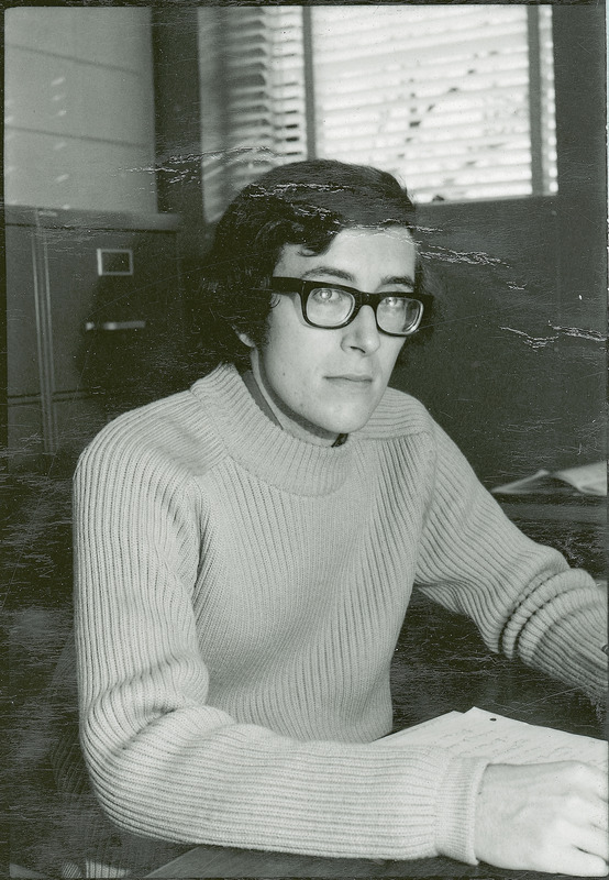 A researcher is seated at a desk with file cabinets in the background.