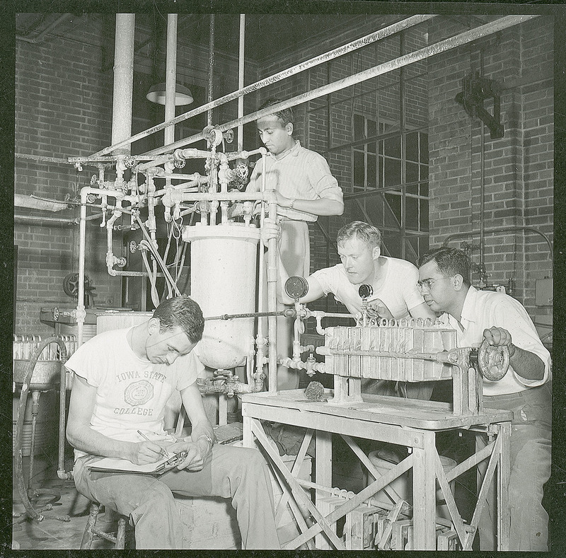 Three men are observing a plate-and-frame-filter press. A fourth individual is recording information on a clipboard. The press, which is used to make filtration tests was introduced to Iowa State University in 1953.