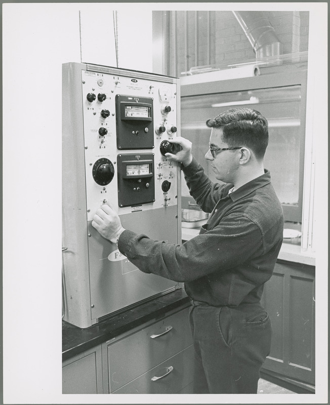 A male researcher is adjusting knobs on a control panel.