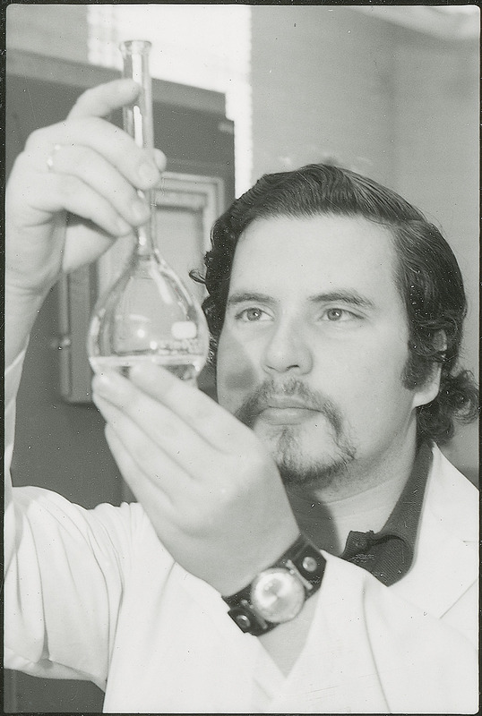 A researcher is studying a liquid contained in a piece of laboratory glassware. This photograph was featured in the Chemical Department's descriptive brochure for 1978.