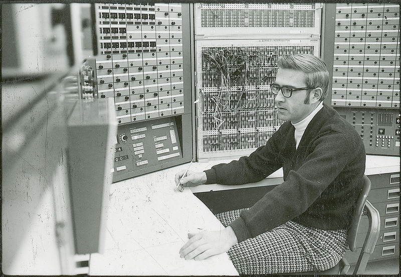 A researcher is sitting at the table surrounded on two sides by various control panels.