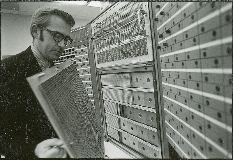 A professor is standing in front of a piece of equipment and holding a large panel. He is examining the inner side of the panel.