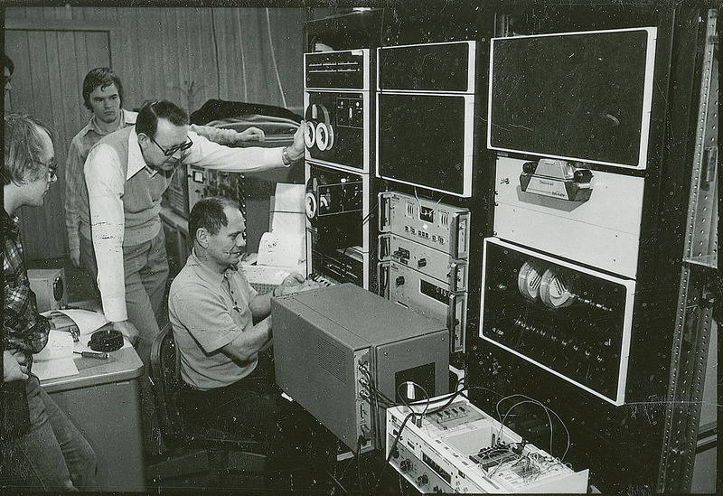 Professor Burkhart and other researchers look on as one individual works with a very early model computer.