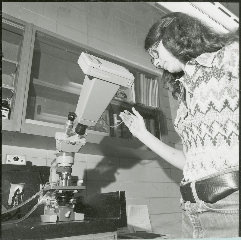 A researcher is taking microscopic photographs using a plunger style remote release. This photograph was featured in the Chemical Engineering Brochure for 1978.